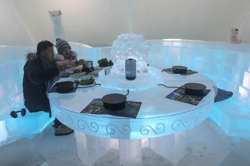 Personas disfrutando de un hotpot en escritorios y sillas tallados en hielo dentro de un iglú.