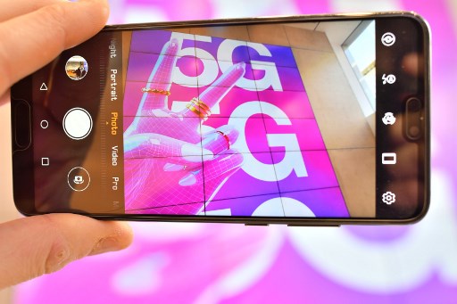 Persona posa sosteniendo un teléfono móvil, la cámara muestra un cartel publicitario de telecomunicaciones móviles 5G en una tienda en Londres.